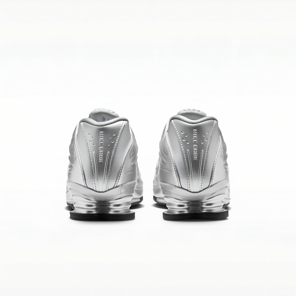 A pair of metallic silver Nike RMX sneakers shown from the back, featuring the 'FIRST STEP' branding and a clear cushioned sole, set against a plain white background.