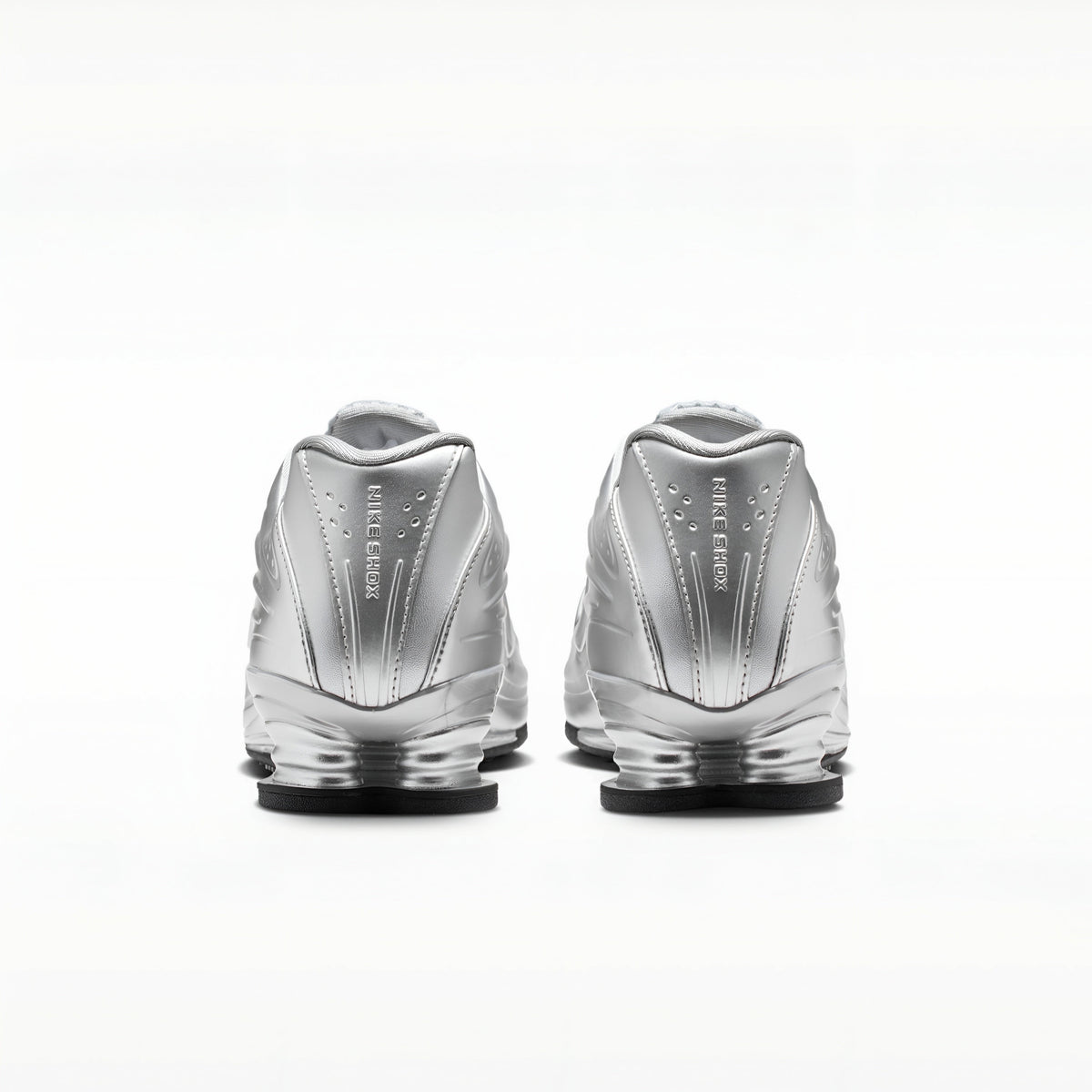 A pair of metallic silver Nike RMX sneakers shown from the back, featuring the 'FIRST STEP' branding and a clear cushioned sole, set against a plain white background.