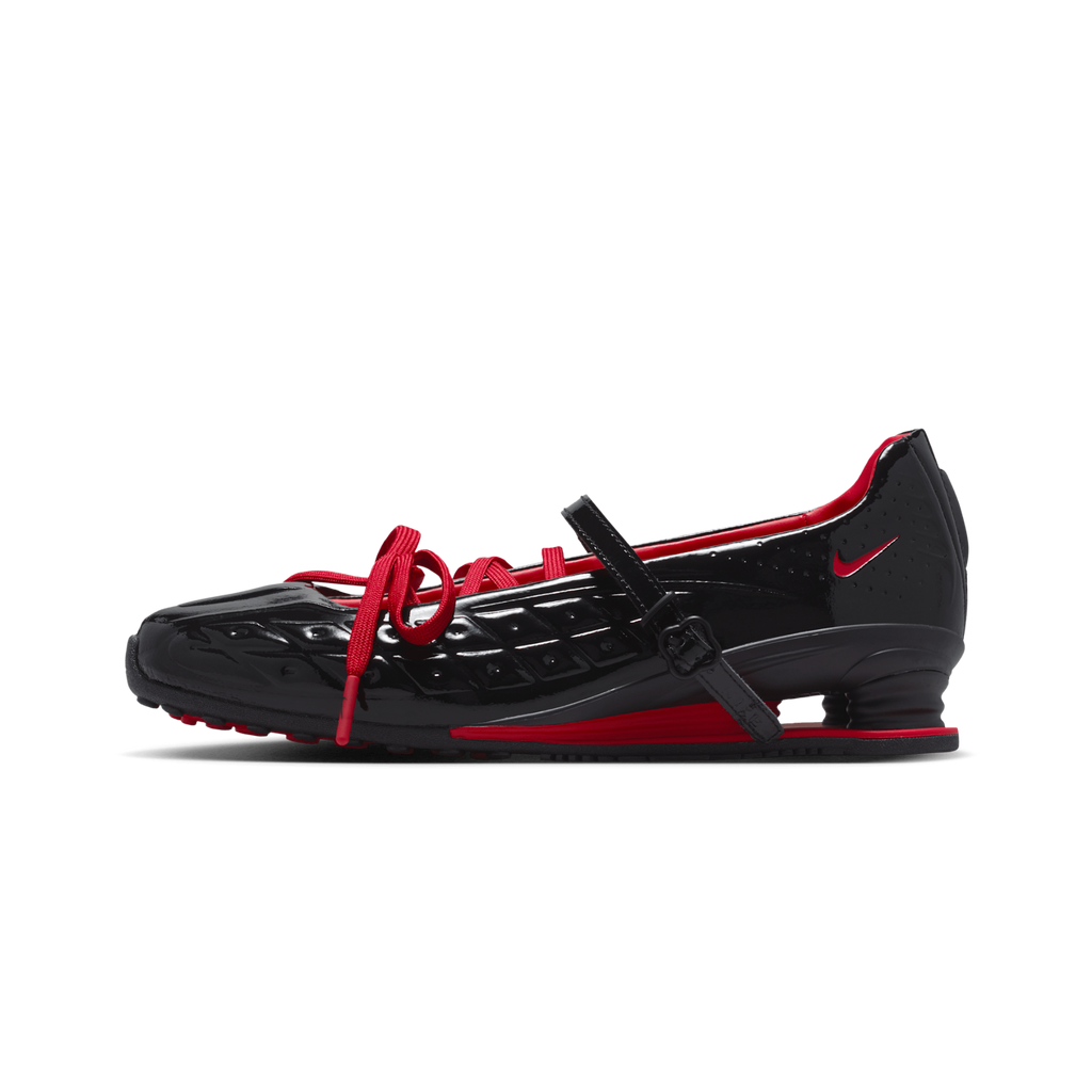 A black Nike shoe with red accents, featuring a glossy textured upper, red laces, a red swoosh, and a red heel counter, shown in a side profile on a white background.